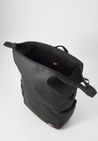 Svart tote-veske med strukturert overflate, glidelåsforsegling, topphåndtak og en utvendig lomme. Innvendig er den tom, med merkeflagg.