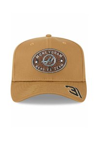 Beige Baseballmütze mit einem gestickten Patch, das das "MoneyGram Haas F1 Team"-Logo in Silber und Kupfer zeigt. Schwarze Akzente an der Seite.