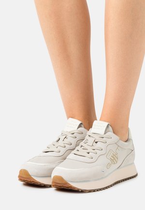 Zapatillas gris claro con materiales de ante y malla, cordones planos y suelas de goma. Presentan un sutil logotipo en el lateral y en la lengüeta.