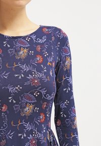 Merenkatu pitkähiha dressi, jossa on kukkakuosit punaisena, keltaisena ja purppurana. Valmistettu pehmeästä kankaasta, jossa on pyöreä kaula-auko ja vartalonmyötäinen siluetti.