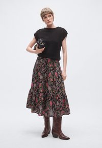 Czarny dziergany top z krótkim rękawem, długa spódnica maxi w czarnym kolorze z kwiatowym wzorem w różowe i zielone akcenty, brązowe kozaki za kolano.