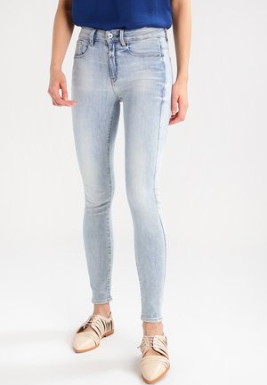 Light blue skinny jeans made of denim, featuring a high waist, subtle fading, and front pockets. Paired with beige lace-up shoes.