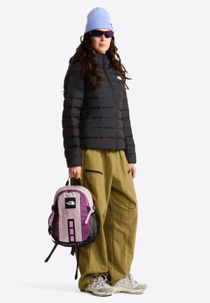 Zwarte donsjas, losse beige broek, paarse en roze rugzak, grijze sneakers, blauwe gebreide muts en zonnebril. Gestructureerd en functioneel ontwerp.