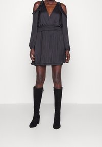 Svart klänning med kallaxel-design, långa ärmar och elastisk midja. Matt textur med en utsvängd kjol. Stylerad med knähöga svarta stövlar.