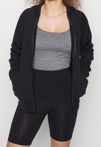 Sudadera negra con cremallera y bolsillos laterales, combinada con una camiseta sin mangas gris y pantalones cortos negros de cintura alta. Textura suave, diseño casual.