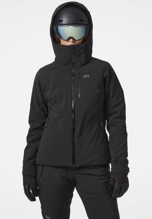 Black ski jacket with a high collar, zippered front, and hood. Features zippered pockets and logo on the chest. Paired with black gloves and pants.