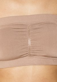 Bež top brez naramnic s smrčenim blagom v središču in elastičnim trakom na dnu. Gladka tekstura in raztegljiv material.