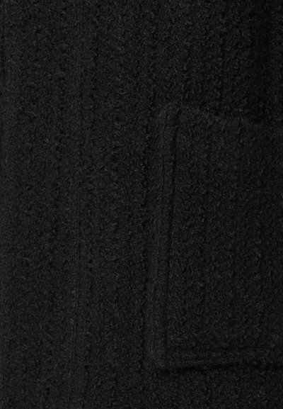 Černý pletený kabát s texturovaným vzorem, který má náprsní kapsu. Materiál vypadá měkký s mírně jemným povrchem.