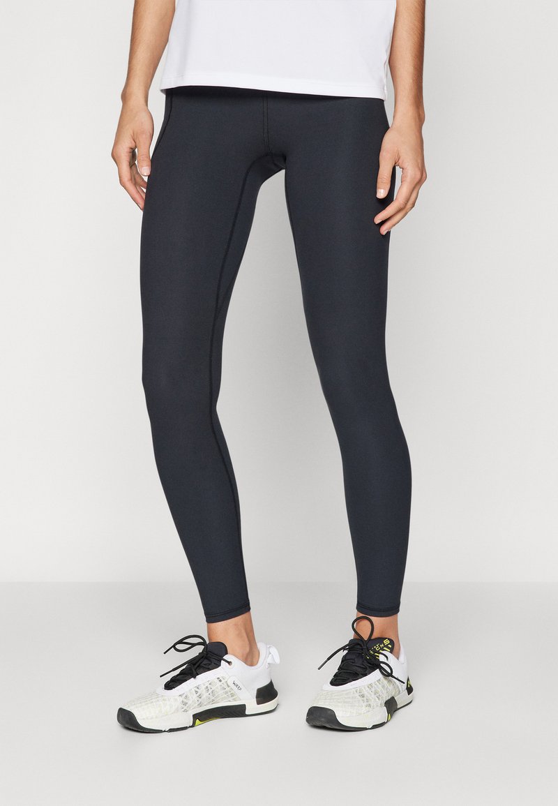 Leggings neri realizzati in materiale elasticizzato, con un design aderente e cuciture senza soluzione di continuità, abbinati a scarpe da ginnastica bianche con accenti neri.