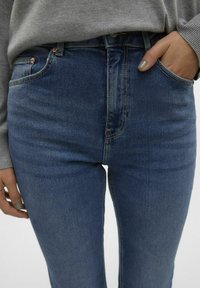 Jean taille haute bleu marine en denim. Caractéristiques : poches avant, détails de couture et texture lisse.