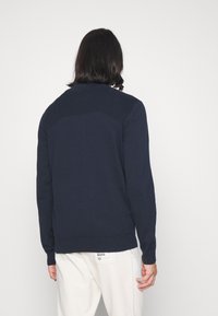 Pull bleu marine avec détails côtelés aux épaules et à l'ourlet, fabriqué en tissu tricoté lisse. Manches longues, dos uni. Design décontracté.