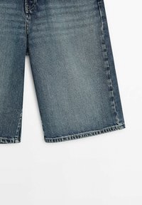 Short en jean d'un bleu moyen avec un aspect délavé et usé et des coutures visibles le long des bords.