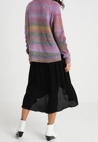 Värikäs neulepaita, jossa on liukuvärinen raidallinen kuvio, pyöreä kaula-aukko ja resorilla viimeistelty helma, yhdistettynä laskeutuvaan mustaan hameeseen.