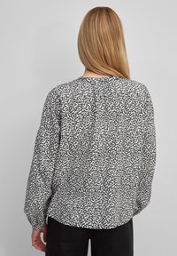 Langarm blouse in zwart-wit gespikkeld patroon, zachte stof, ontspannen pasvorm, ronde halslijn en geplooide detail achter.