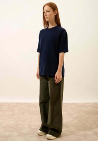 Granatowa, krótko rękawowa, oversize'owa koszula uszyta z miękkiego materiału, w połączeniu z szerokimi, ciemnozielonymi spodniami i jasnymi trampkami.