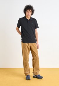 Black short-sleeve polo shirt with a subtle logo, paired with light brown corduroy pants and dark sneakers. Simple and functional outfit.