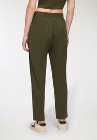 Pantaloni verde oliva con vita elastica presentano una vestibilità rilassata e gambe affusolate, realizzati in tessuto morbido, abbinati a sneakers di colore neutro.