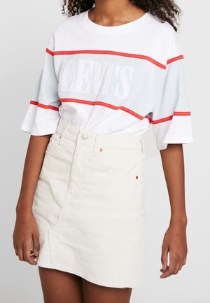 Biała, oversize'owa koszulka z czerwonymi i niebieskimi poziomymi paskami, z logo "LEVI'S"; zestawiona z jasnobeżową mini spódnicą z kordurowej tkaniny z kieszeniami.