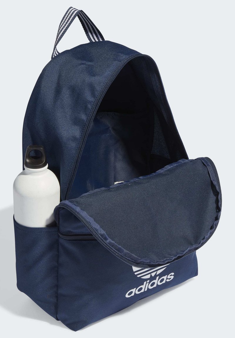 Zaino blu navy realizzato in tessuto resistente, dotato di una patta frontale, comparto con zip e una tasca laterale con una bottiglia d'acqua bianca.
