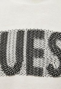 Maglione a maglia che presenta un tessuto bianco con un grande pattern di testo nero, caratterizzato da un design a strisce orizzontali testurizzate.