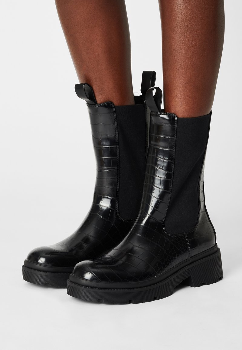 Black ankle boots with a crocodile texture, elastic side panels, and pull tabs. Features a thick black sole for added support and stability.