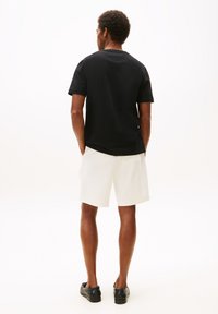 T-shirt noir à manches courtes avec un col rond, associé à un short blanc et des baskets noires. Le matériau semble lisse et léger.