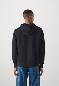 Felpa con cappuccio di colore blu navy in morbido tessuto, caratterizzata da una vestibilità comoda, polsini a coste e orlo piatto, abbinata a pantaloni cargo in denim.