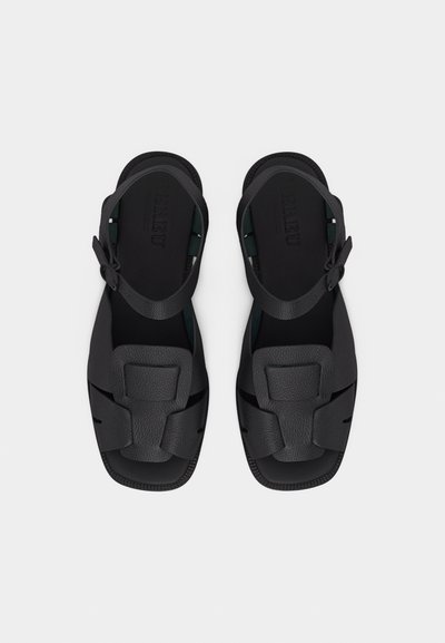 Sandales en cuir noir avec des brides ajustables à la cheville et un large design découpé sur le dessus, vues de dessus sur un fond blanc.