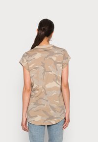 Camiseta de camuflaje en tono marrón con mangas cortas, dobladillo redondeado y una textura suave. Presenta una etiqueta de marca discreta en la parte posterior.