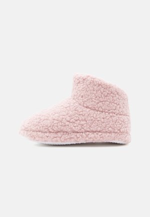 Rózsaszín bolyhos papucs puha, texturált felülettel, kerek orral és alacsony bokarészes kialakítással. Fehér gumi talppal rendelkezik a tapadás érdekében.