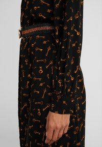 Czarna sukienka z długim rękawem z wzorem pomarańczowych kluczy. Podkreślona teksturowanym czarnym paskiem z połyskiem i złotym zapięciem.