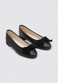 Ballerines en cuir noir avec un bout arrondi, ornées d'un nœud contrastant à l'avant et d'un petit talon. Texture lisse sur toute la surface.