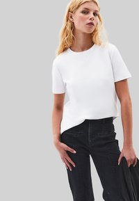 Haut blanc à manches courtes avec un décolleté rond, associé à un pantalon noir taille haute avec poches avant et une finition en tissu texturé.