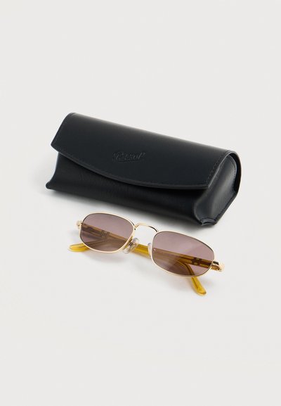 Ορθογώνια γυαλιά ηλίου με χρυσά πλαίσια και καφέ φακούς, τοποθετημένα δίπλα σε μαύρη δερμάτινη θήκη με ανάγλυφο το όνομα της επωνυμίας.