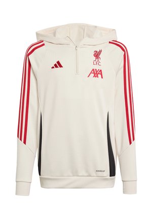 To unge mennesker iført hvide Liverpool FC-hoodies med røde striber og sorte bukser står mod en ensfarvet baggrund.