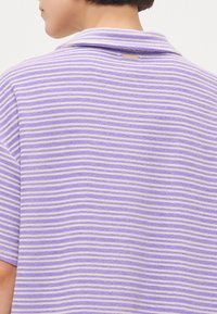 Camicia a maniche corte con righe alternate in lavanda e beige. Tessuto morbido con colletto classico e un piccolo tag del marchio sul retro.