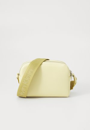Yellow faux leather crossbody bag with a textured finish and adjustable fabric strap featuring a logo. Compact rectangular shape.