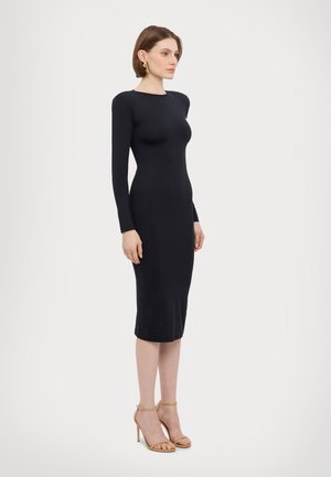 Black, form-fitting midi dress with long sleeves and round neckline, made of smooth fabric; model paired with nude strappy high heels.