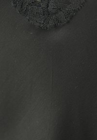 Schwarzer Stoff mit einer glatten Textur, der oben mit einer Spitzenakzent versehen ist. Das Material erscheint leicht und leicht glänzend.