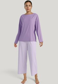 Paarse lange mouwtop met een brede halslijn, gecombineerd met geruite lavendel en witte wijde broek. Zacht materiaal en een losjes zittende pasvorm.