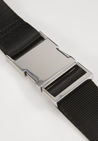Sangle en nylon noir avec boucle en métal argenté brillant attachée, présentée sur un fond clair uni.