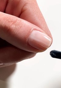 Nagel med en glansig, ombre-finish som har ljusrosa och nudetoner. En pensel är redo nära fingertoppen för applicering.