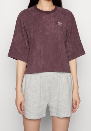 Fioletowy zamszowy krótki top z krótkimi rękawami i okrągłym dekoltem, w połączeniu z jasnoszarymi szortami dresowymi z elastycznym pasem.