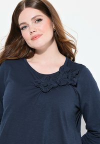Mörkblå långärmad topp med tygblommor på vänster axel. Mjuk textur med rund halsringning och avslappnad passform.