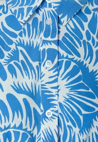 Korte mouw blouse in lichtblauw en wit, met een gedurfde, abstracte print. Gemaakt van gladde stof met een puntige kraag en knoopsluiting.