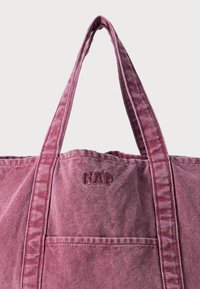 Canvas tote bag in a muted burgundy color with sturdy dual handles, visible stitching, and a front pocket featuring embossed "GAP" logo.