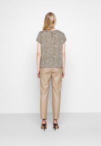 Blouse à motifs texturés marron et blanc avec manches courtes, associée à un pantalon en cuir beige effilé et des talons noirs à lanières, vue de dos.