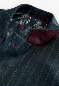 Blazer en denim foncé avec un motif rayé, accent de col bordeaux, doublure intérieure fleurie, tissu texturé et détails de coupe ajustée.