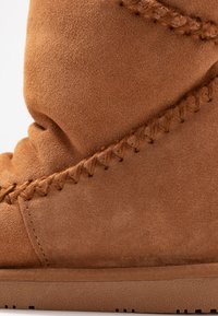 Bottine en suède marron avec un surpiquage décoratif, une surface texturée et une semelle en caoutchouc durable présentant un motif texturé.