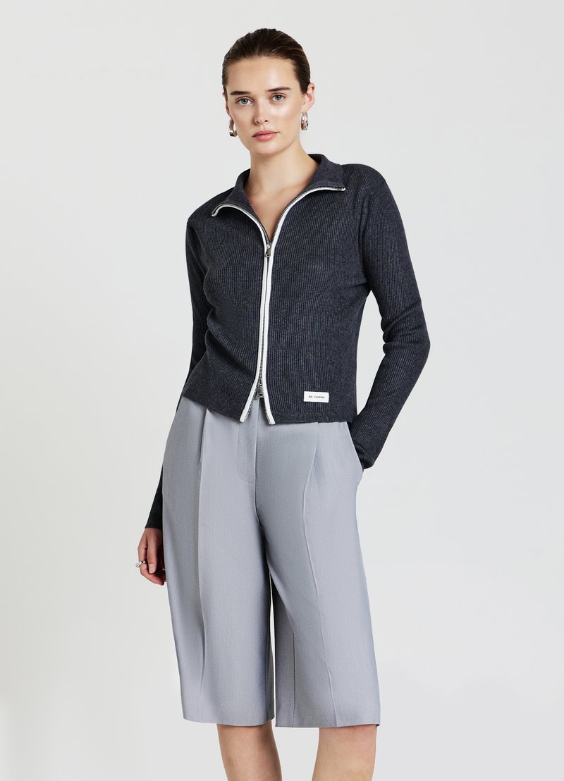 Veste zippée noire côtelée avec des détails de fermeture éclair blancs, associée à un short ample gris clair. Les deux vêtements présentent des textures lisses.